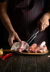 Preparation for cooking veal meat ribs by the hands of the chef in the kitchen of the restaurant. The chef's hand is holding a fork. Delicious grilled lunch.