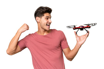 Young caucasian man holding a drone over isolated background celebrating a victory