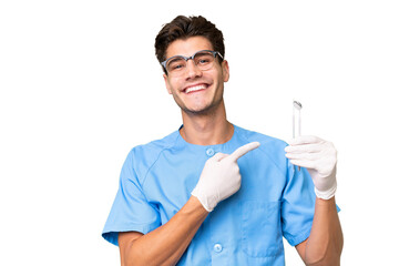 Young dentist man holding tools over isolated background pointing to the side to present a product - obrazy, fototapety, plakaty