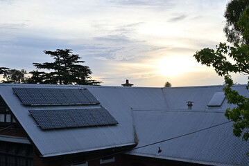Solar panels in the shade on a tin roof, or corrugated iron, with the sun setting in the background