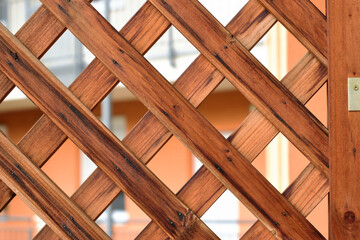 Brown wood trellis macro. pine wood privacy screen or lattice detail. narrow strips fastened with small metal nails. diamond shape pattern. flat brown wood strips. soft blurred residential background