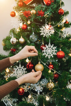 Young woman's hand decorating Christmas tree indoors.