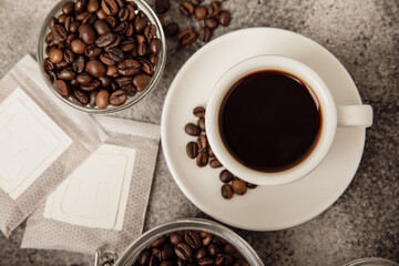 Drip coffee bags, coffee beans and a white cup on a texture table. Ground coffee for brewing in a cup, paper bag drip coffee filter packaging. Place to copy. Place for text.