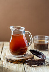 Healthy immune carob molasses beverage in glass jar, carob pod, molasses on wooden and brown...
