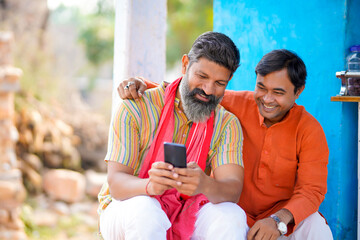 Indian farmer showing some detail to his friend in smartphone at home.