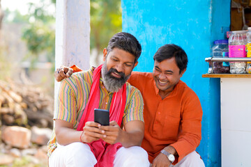 Indian farmer showing some detail to his friend in smartphone at home.