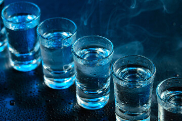 Wet glasses of vodka in smoke on dark blue background.