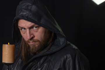 Portrait of a man in a cloak with a hood against a dark background with a candle on candlestick