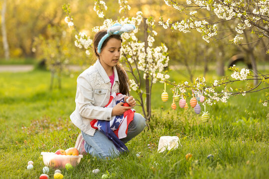 A teenage girl in a blooming garden at Easter with a US flag