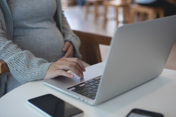 Pregnant woman working on laptop. Cropped image of pregnant businesswoman sitting at table typing...