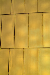 Metallic panneling on the side of building or business with metal wires and square tiles in an urban area of the city in afternoon light