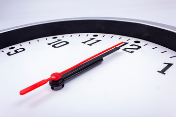 Midnight is coming. Black and white office clock with a red pointer on a gray background.