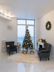 Beautiful light interior of living room with decorated Christmas tree and gifts. Candles on fireplace. Wreath on brick wall. Two cozy armchairs.