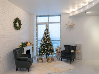 Beautiful light interior of living room with decorated Christmas tree and gifts. Candles on fireplace. Wreath on brick wall. Two cozy armchairs.