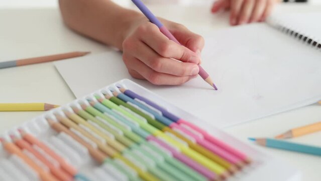 Child hand drawing with crayons from coloful palette on white paper. Person kid painting with pencils in album