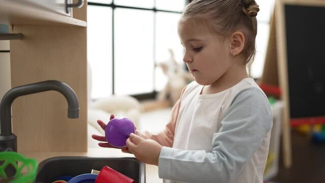 Adorable hispanic girl playing with play kitchen standing at kindergarten