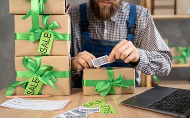 male small business owner in leprechaun hat checking parcel box, glue barcode. Warehouse worker,...
