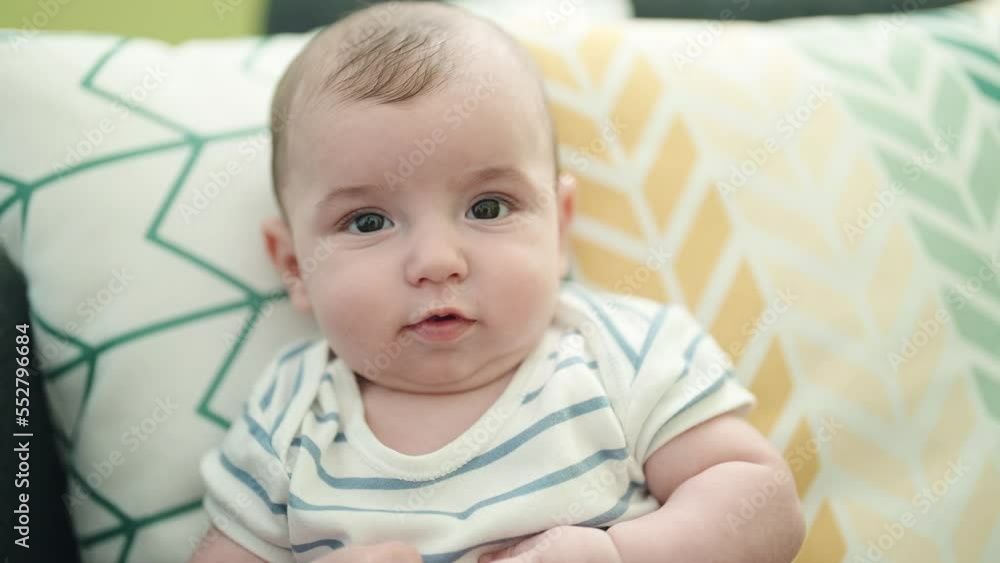 Sticker Adorable caucasian baby smiling confident sitting on sofa at home