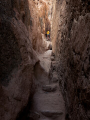Woman walks through dark narrow canyon with rough vertical stone walls, Dahab, Egypt