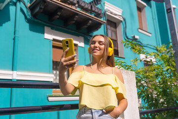 Summer lifestyle, blonde woman in a house with a green colorful facade, music online with the phone