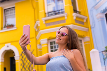 Portrait attractive young blonde woman taking a photo, behind yellow and blue colorful facade