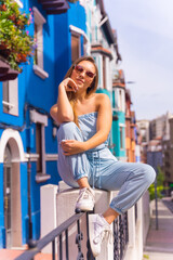 Portrait of attractive young blonde woman in sunglasses smiling, behind blue colorful facade