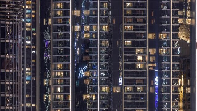 Night view of many glowing windows in apartment building timelapse. High rise skyscraper with lights in rooms. Evening illumination