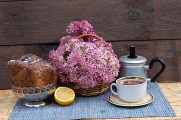  a cup of tea , a lemon, a cupcake , a basket of pink flowers and a teapot.