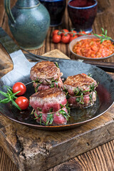 Traditional barbecue dry aged angus medaillon beef filet steak natural with herbs tomatoes served as close-up in a rustic wrought iron frying pan