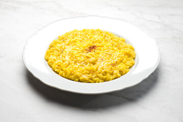 Close-up of risotto alla Milanese  in a white aristocratic dish on a white marble background. A classic Lombard saffron risotto recipe. Cuisine of the north Italy, front view