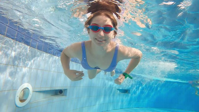 Smilling girl with goggles diving and swimming underwater in a pool