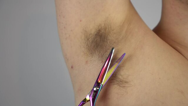 A young man cuts long hair in his armpit with hairdressing scissors. Bodypositive man doing armpit haircut.