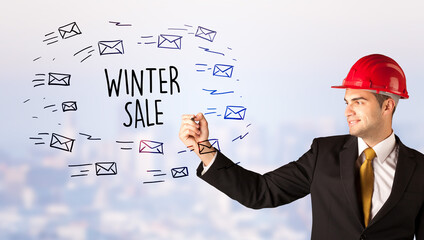 Young businessman with helmet drawing sale sign