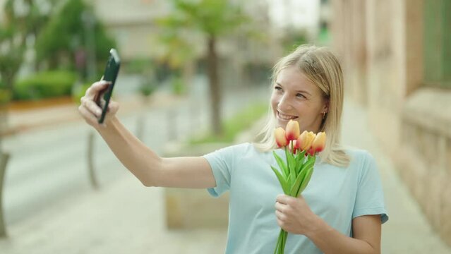 Young blonde woman make selfie by smartphone holding bouquet of flowers at street