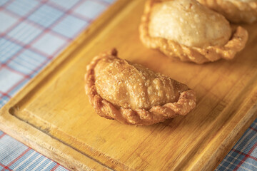 Close up of fried Argentine empanadas on a wooden board and checkered tablecloth.
