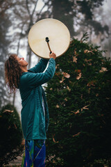 shamanic woman playing on shaman frame drum in the nature.