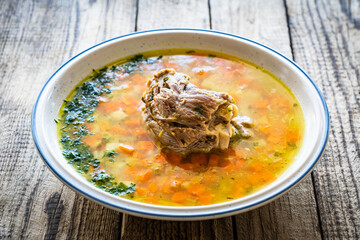 Fresh spring soup with big piece of meat on wooden table