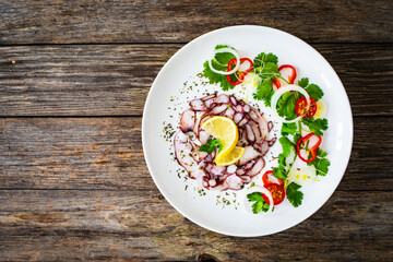 Octopus carpaccio with lemon and greens on wooden table
