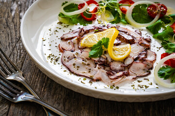 Octopus carpaccio with lemon and greens on wooden table
