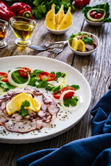 Octopus carpaccio with lemon and greens on wooden table
