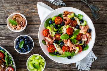 Fresh salad - prosciutto Crudo, pear, tomatoes and leafy vegetables on wooden table
