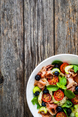 Fresh salad - prosciutto Crudo, pear, tomatoes and leafy vegetables on wooden table

