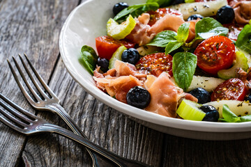 Fresh salad - prosciutto Crudo, pear, tomatoes and leafy vegetables on wooden table
