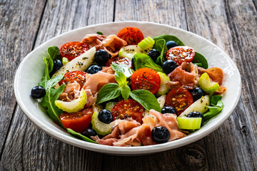 Fresh salad - prosciutto Crudo, pear, tomatoes and leafy vegetables on wooden table

