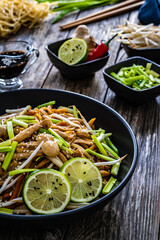 Asian food - Chow Mein noodles, stir fried vegetables, soy sauce and shimeji mushrooms on wooden table
