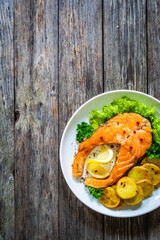 Fried salmon steak with potatoes and fresh vegetable salad served on wooden table
