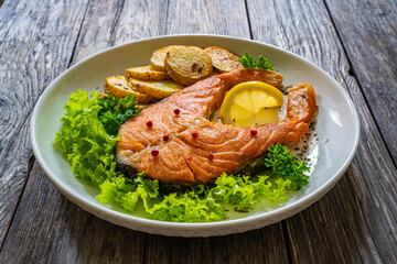 Fried salmon steak with potatoes and fresh vegetable salad served on wooden table
