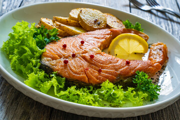 Fried salmon steak with potatoes and fresh vegetable salad served on wooden table
