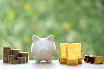 Piggy bank with gold bar and stack of coins money on natural green background,Business investment...