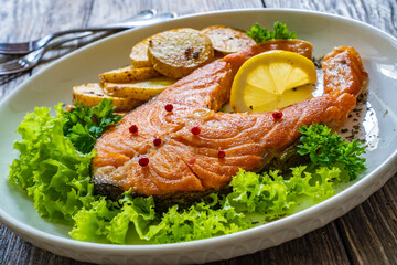 Fried salmon steak with potatoes and fresh vegetable salad served on wooden table
